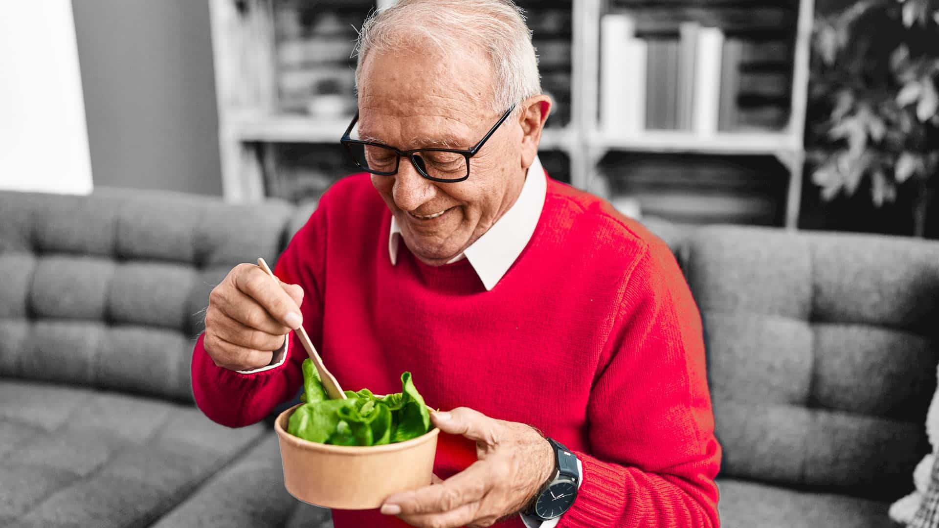 older man eating salad from a bowl while seated on a couch