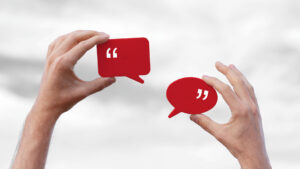 two hands holding red speech bubble blocks up against the backdrop of the sky